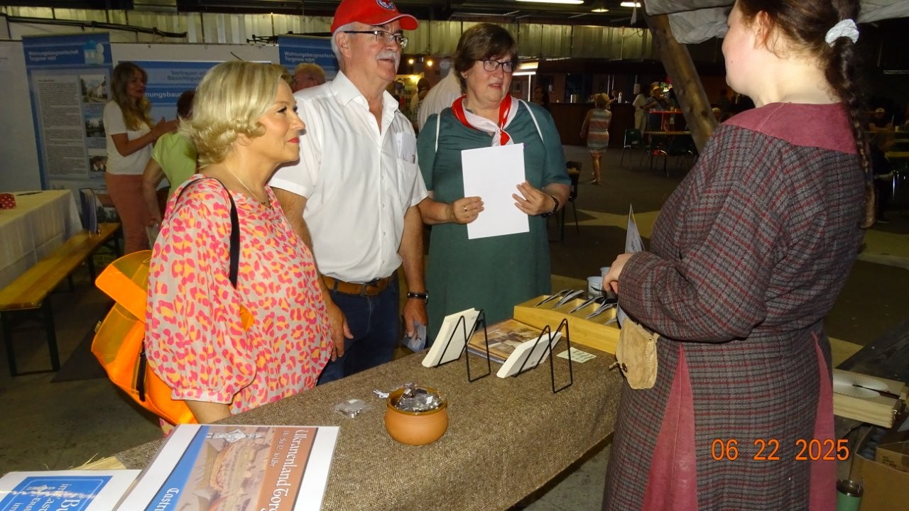 Vier Personen unterhalten sich an einem Tisch mit Broschüren in einer Messehalle.