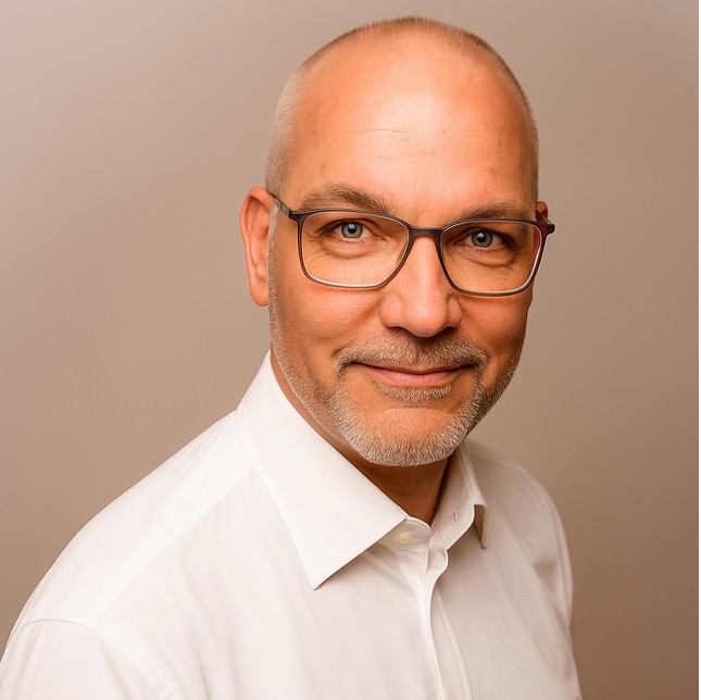 Mann mittleren Alters, Glatze, Brille, weißes Hemd, lächelt, neutraler Hintergrund.