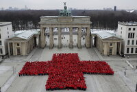Menschen in roten Kleidern bilden ein großes rotes Kreuz vor dem Brandenburger Tor in Berlin