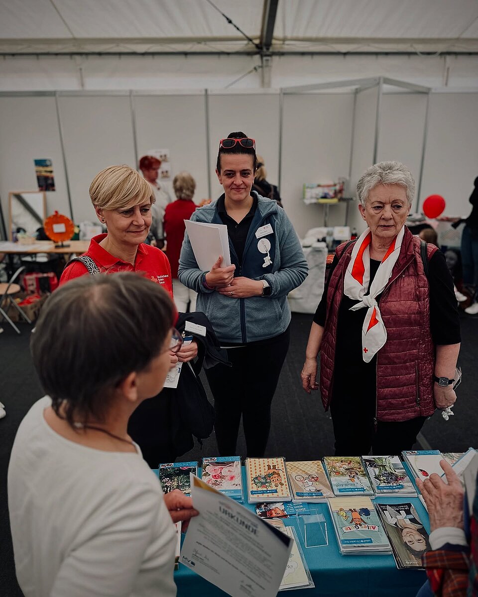 Vier Frauen unterhalten sich an einem Tisch mit Broschüren und Karten in einem Ausstellungszelt.