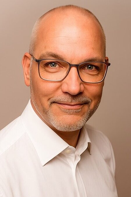 Mann mittleren Alters, Glatze, Brille, weißes Hemd, lächelt, neutraler Hintergrund.