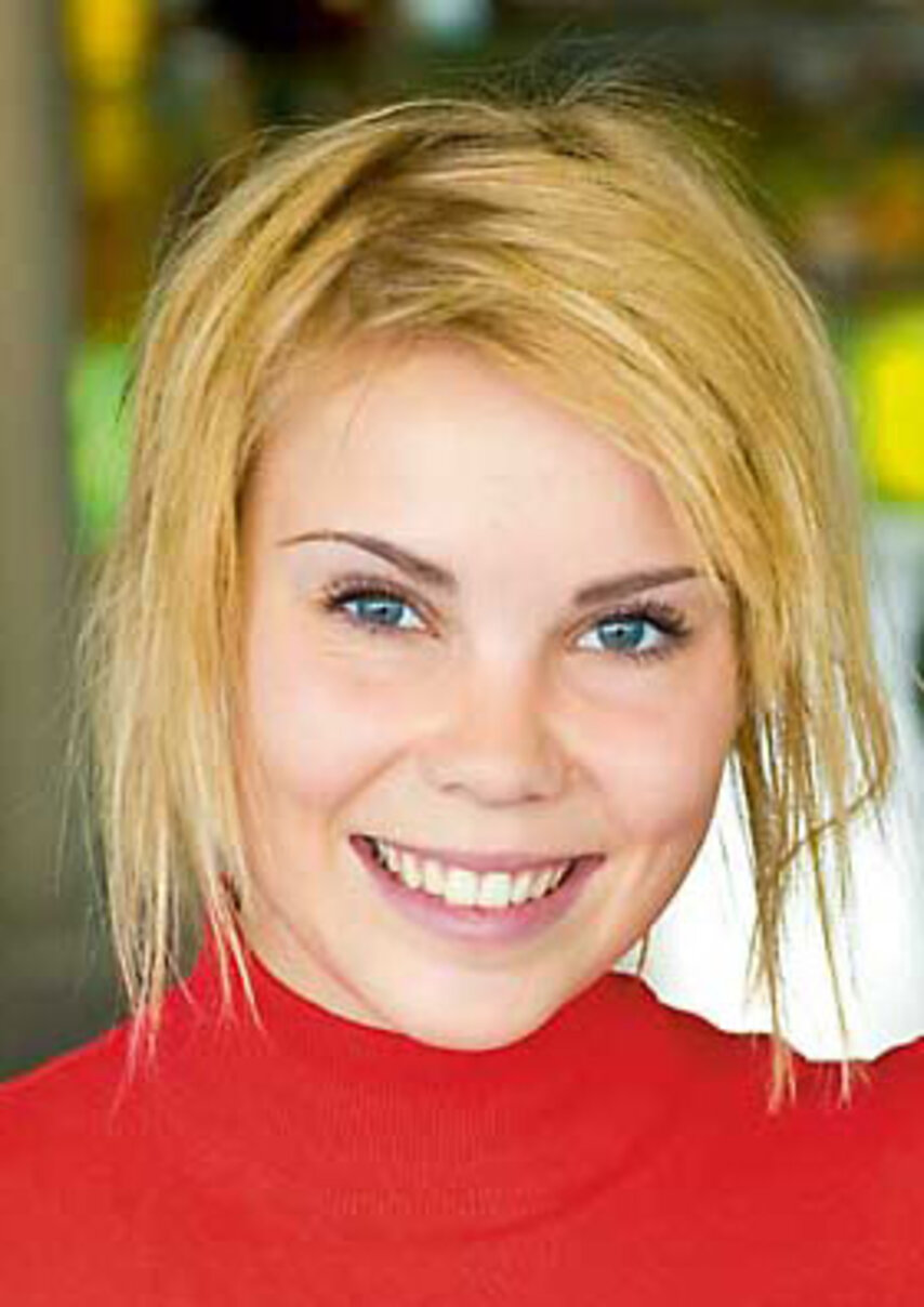 Person mit blonden Haaren und rotem Oberteil lächelt in die Kamera.