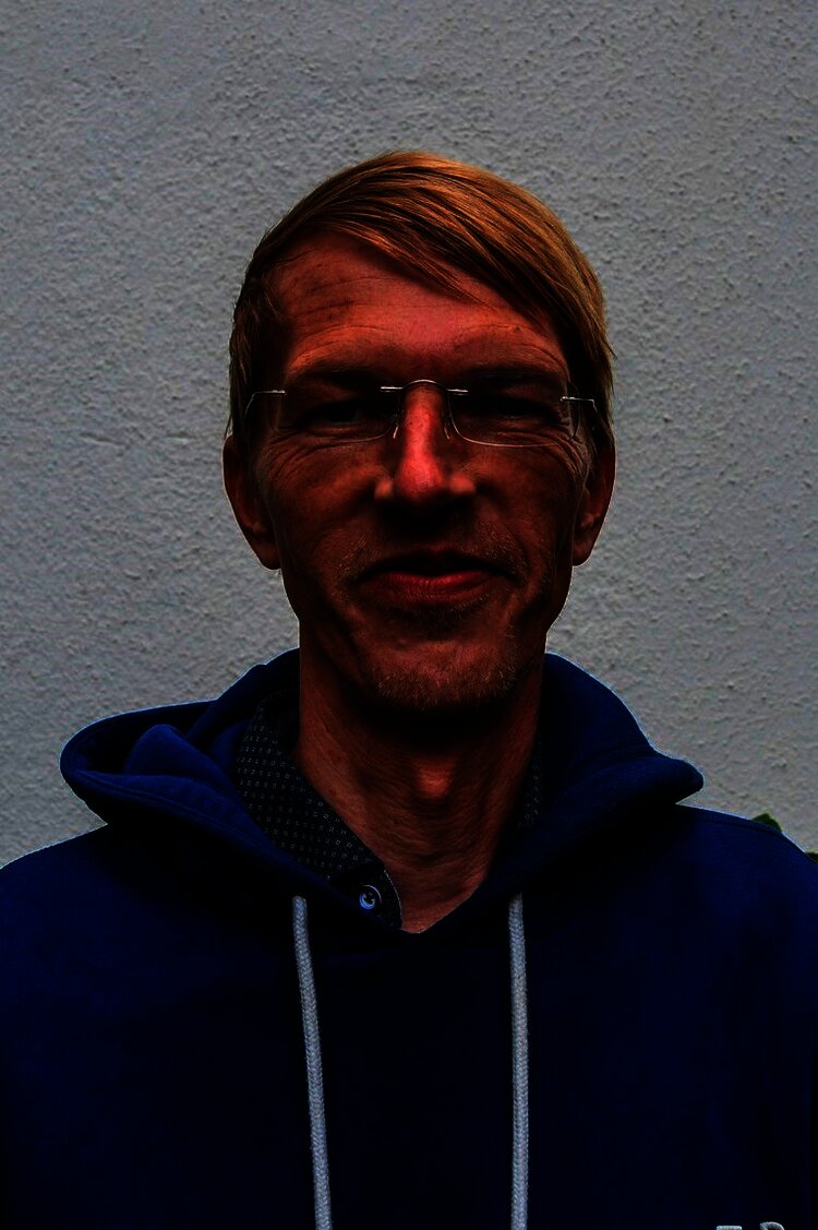 Person mit Brille und blauem Hoodie lächelt vor neutralem Hintergrund.