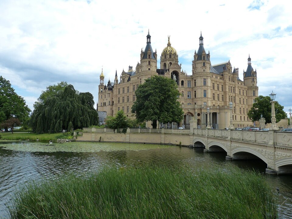 Schloss mit goldener Kuppel und Türmen, von Bäumen umgeben, neben einem See und einer Steinbrücke.