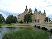 Schloss mit goldener Kuppel und Türmen, von Bäumen umgeben, neben einem See und einer Steinbrücke.