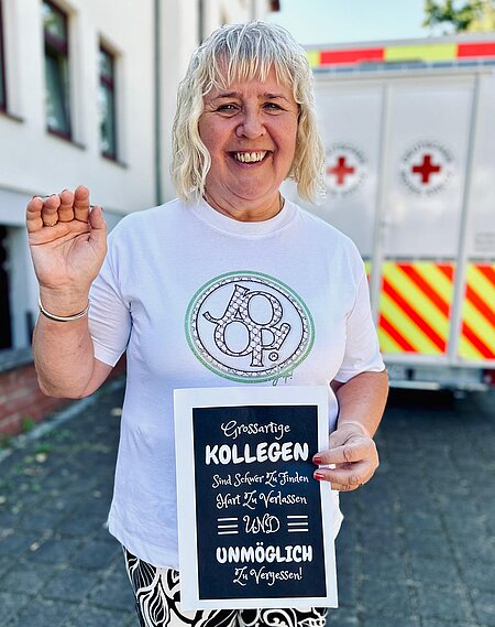 Lächelnde Person hält Schild mit Text: „Großartige Kollegen sind schwer zu finden, hart zu verlassen und unmöglich zu verg...