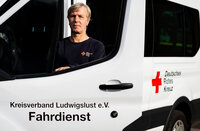 Person in einem weißen Fahrzeug des Deutschen Roten Kreuzes, Aufschrift "Kreisverband Ludwigslust e.V. Fahrdienst".