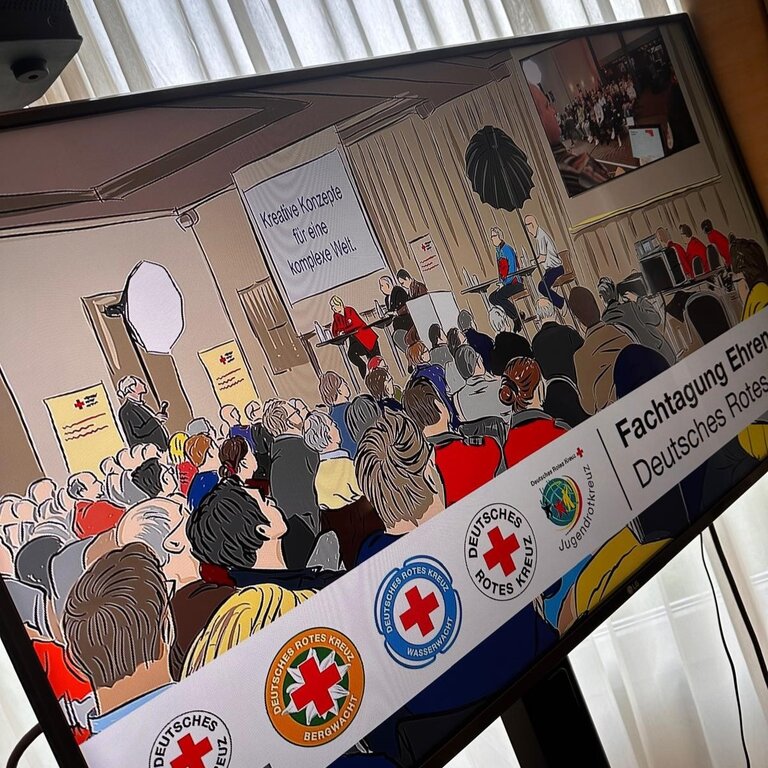 Menschen bei einer Konferenz des Deutschen Roten Kreuzes, Banner mit Slogan und Logos sichtbar.