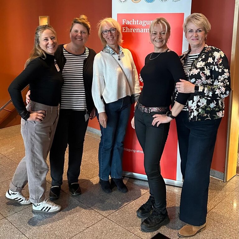 Fünf Personen stehen lächelnd vor einem Banner mit der Aufschrift "Fachtagung Ehrenamt" in einem Innenbereich.